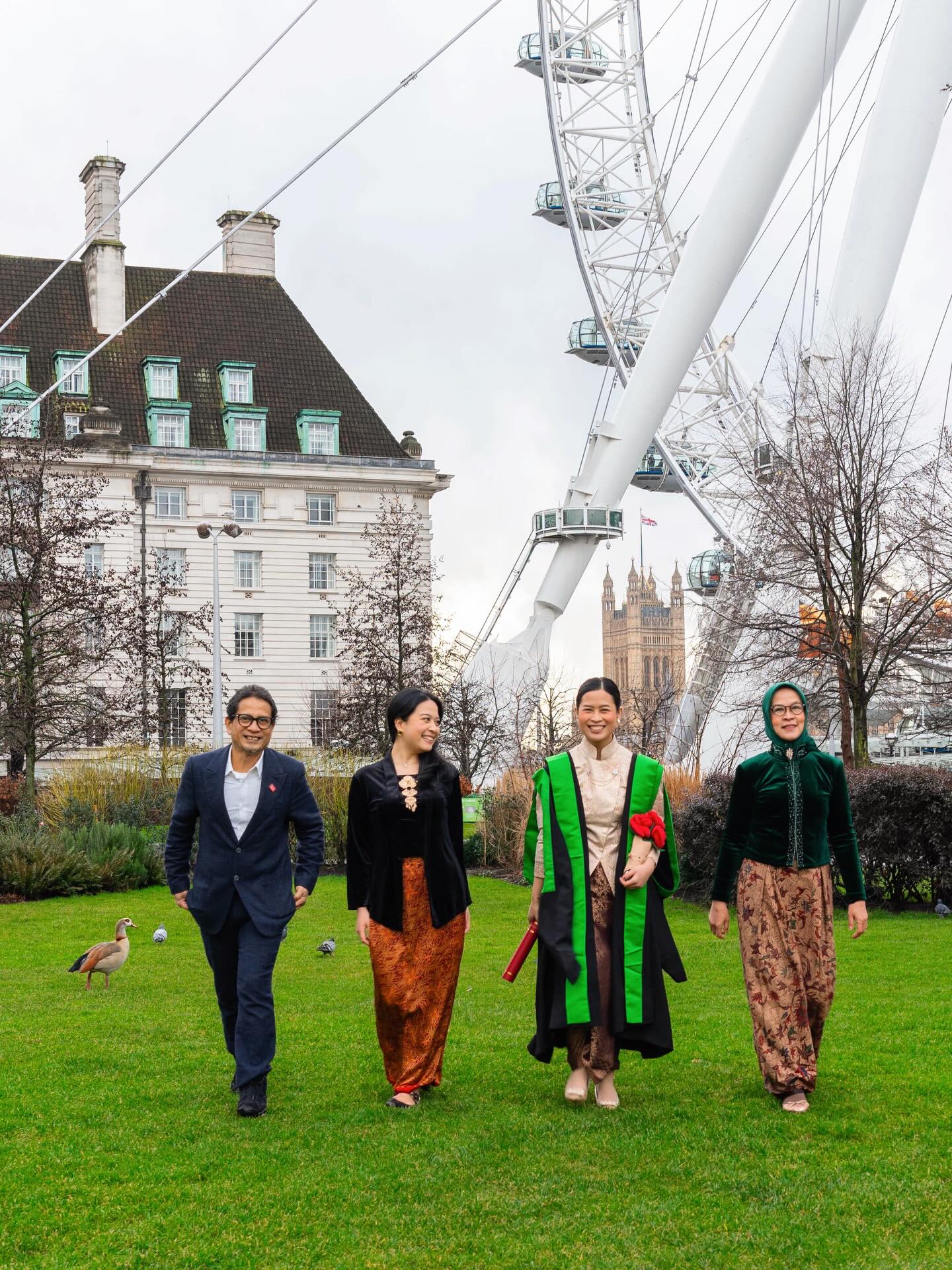 Graduate in green academic hood walking with family near the London Eye, wearing traditional Indonesian batik and kebaya