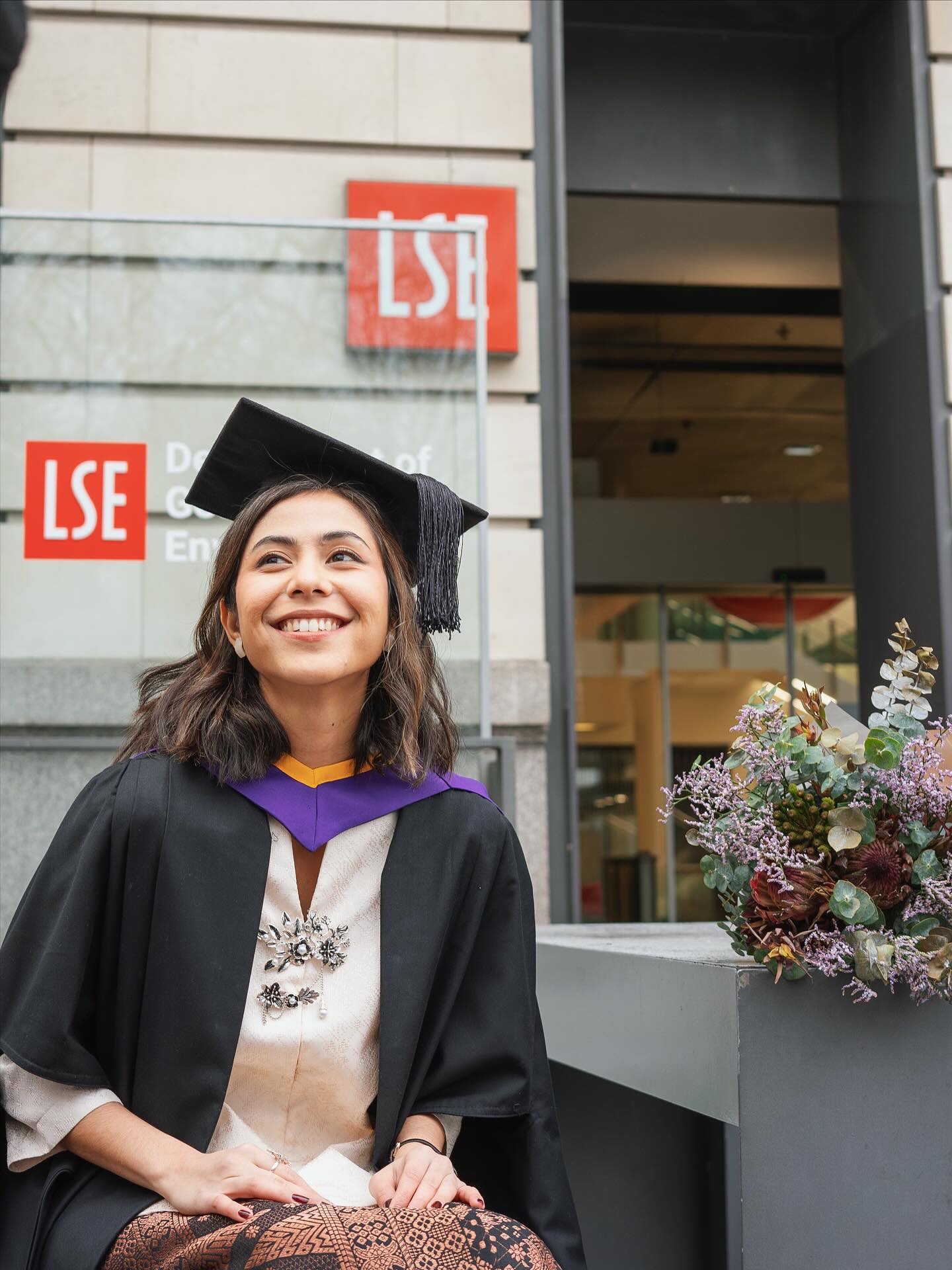 LSE graduate in cap and gown outside the London School of Economics building