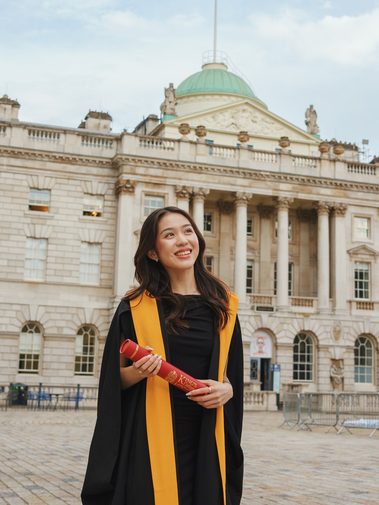 King's College London graduate holding her degree scroll in the courtyard at Somerset House, London