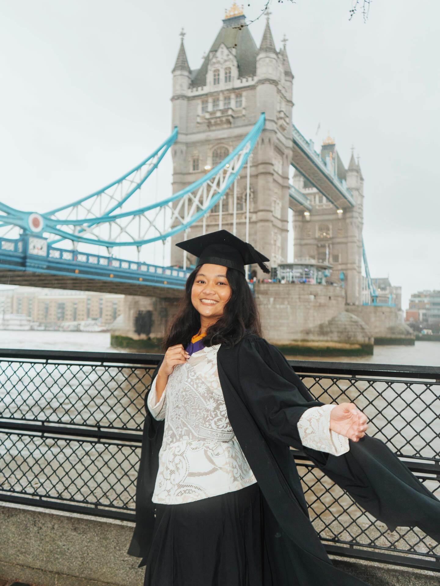 Graduate in academic gown posing in front of Tower Bridge, London