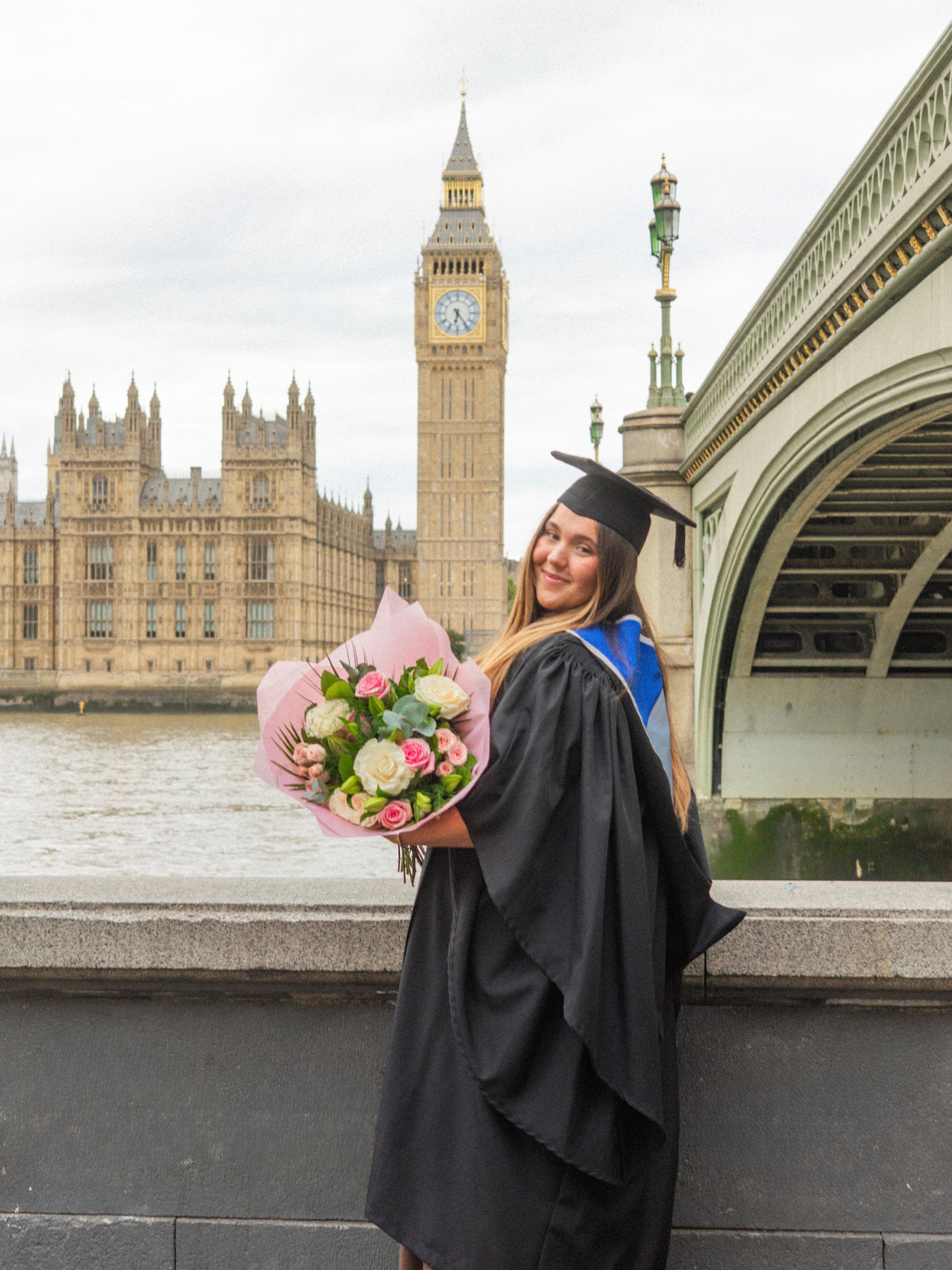 Graduate holding flowers on Westminster Bridge with Big Ben and the Houses of Parliament in the background